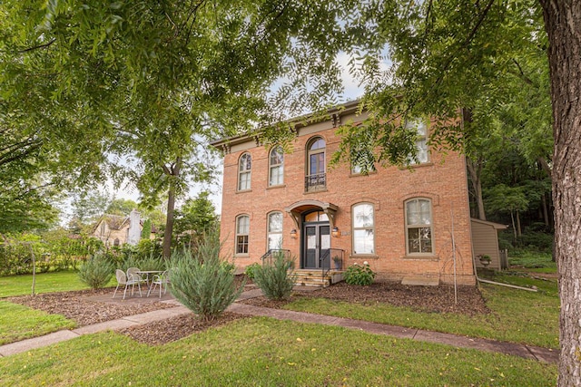 italianate house with brick siding, a patio area, and a front yard