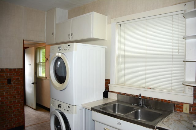 laundry area featuring sink, stacked washer / dryer, cabinets, and light tile floors