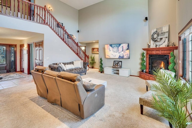 carpeted living room featuring stairs, a glass covered fireplace, a high ceiling, and baseboards