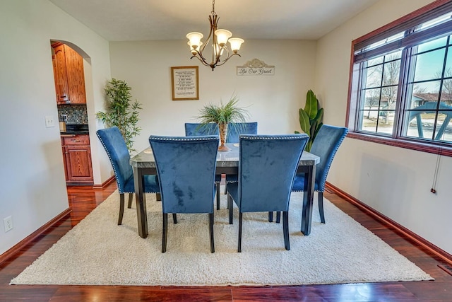 dining space with dark wood finished floors, a chandelier, arched walkways, and baseboards