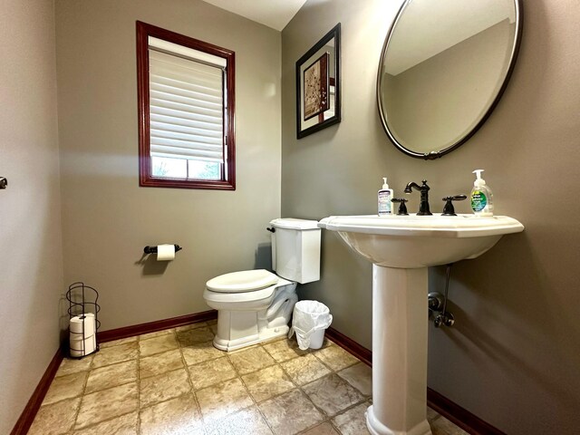 half bathroom featuring stone finish floor, toilet, and baseboards