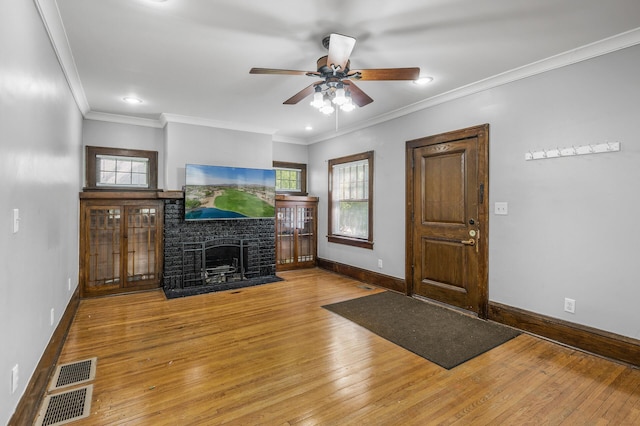 entrance foyer featuring wood-type flooring, crown molding, ceiling fan, and a brick fireplace