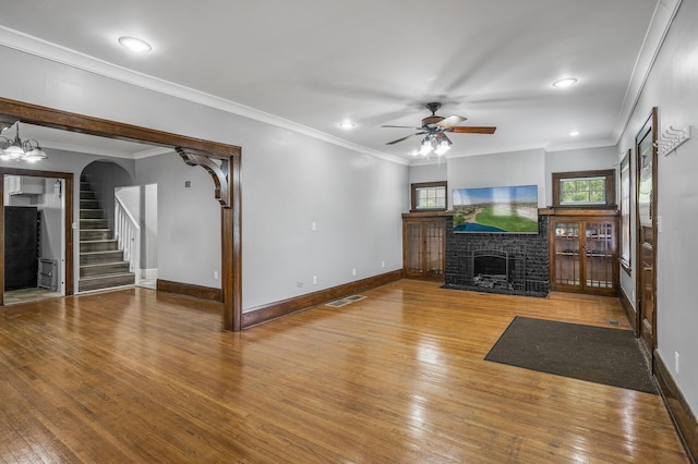 unfurnished living room featuring a brick fireplace, ceiling fan with notable chandelier, crown molding, and wood-type flooring