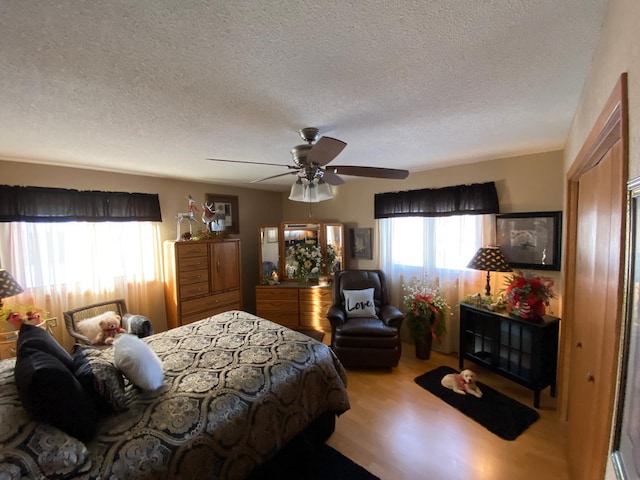 bedroom with ceiling fan, light wood-type flooring, and a textured ceiling