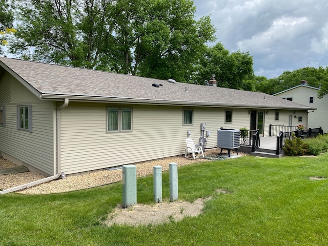 rear view of property featuring a wooden deck, cooling unit, a lawn, and roof with shingles