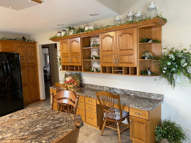 kitchen featuring open shelves, built in study area, freestanding refrigerator, and brown cabinets