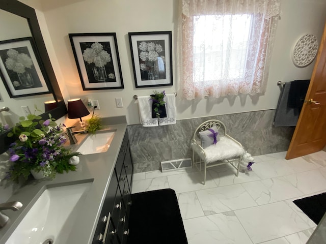 full bath with double vanity, visible vents, wainscoting, marble finish floor, and a sink