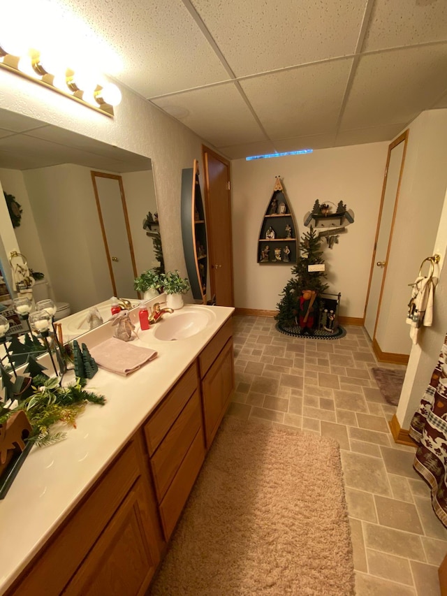 bathroom with a paneled ceiling, stone finish floor, vanity, and baseboards