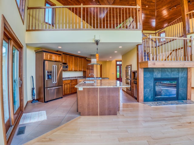 kitchen with a high ceiling, appliances with stainless steel finishes, extractor fan, decorative light fixtures, and sink