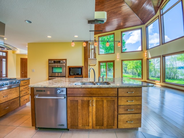 kitchen featuring an island with sink, appliances with stainless steel finishes, light tile patterned flooring, light stone counters, and sink