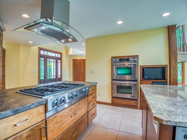 kitchen with a textured ceiling, a center island, island exhaust hood, stainless steel appliances, and light tile patterned flooring