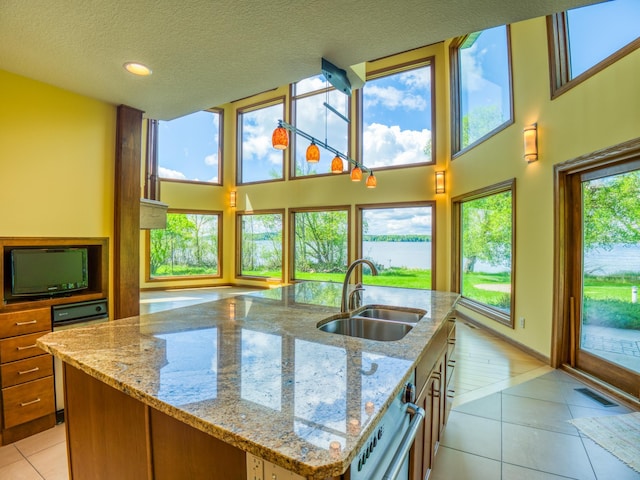 kitchen with light tile patterned flooring, a kitchen island with sink, light stone counters, and sink