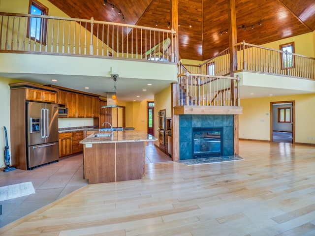 kitchen with pendant lighting, a high ceiling, light wood-type flooring, appliances with stainless steel finishes, and an island with sink