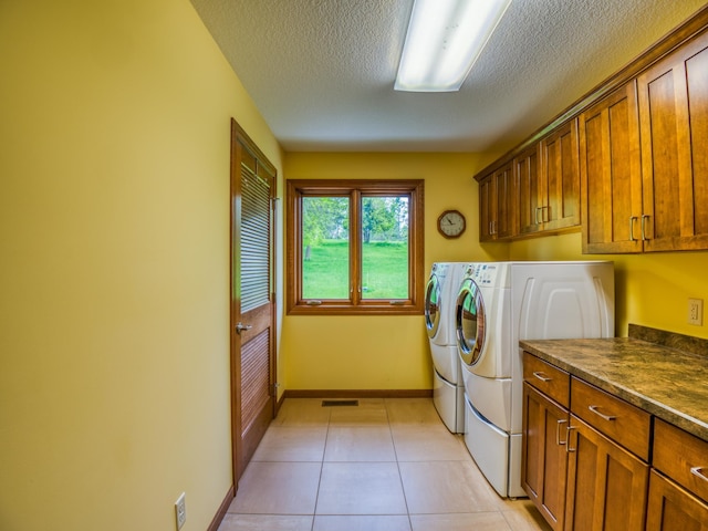 washroom featuring washer and clothes dryer, light tile patterned flooring, a textured ceiling, and cabinets