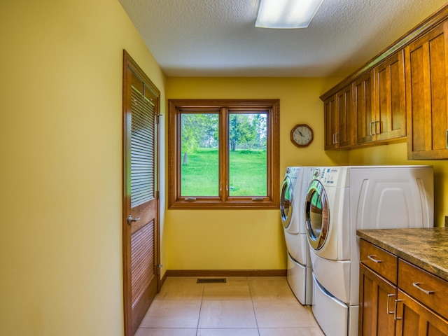 laundry room with light tile patterned floors, washer and dryer, a textured ceiling, and cabinets