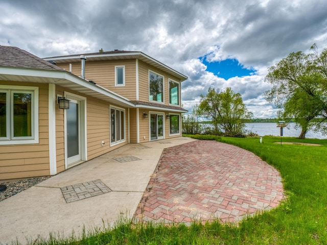 rear view of property featuring a lawn, a water view, and a patio