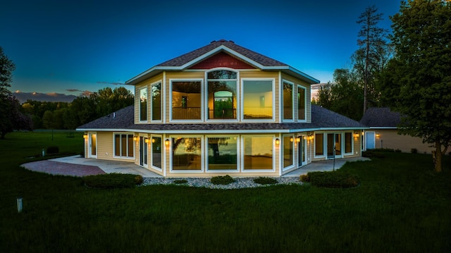 back house at dusk featuring a patio area and a yard