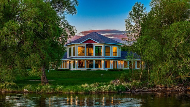 back house at dusk featuring a water view and a lawn