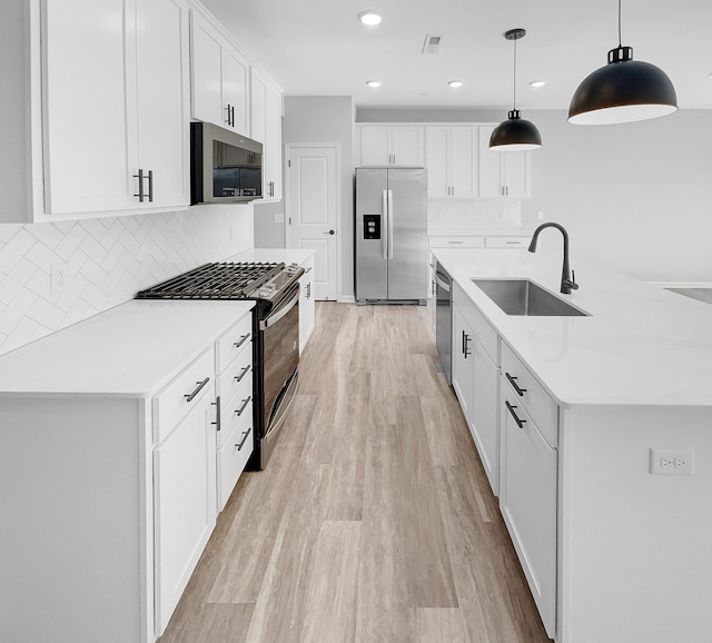 kitchen with appliances with stainless steel finishes, light wood-type flooring, sink, white cabinetry, and hanging light fixtures