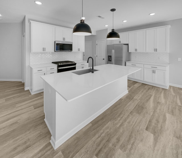 kitchen with appliances with stainless steel finishes, a center island with sink, white cabinetry, and sink