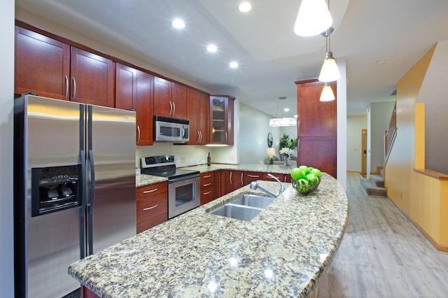 kitchen with appliances with stainless steel finishes, pendant lighting, sink, light stone counters, and kitchen peninsula