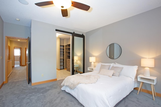 carpeted bedroom with a walk in closet, a closet, ceiling fan, and a barn door