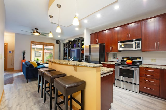 kitchen with light hardwood / wood-style flooring, a breakfast bar area, appliances with stainless steel finishes, hanging light fixtures, and an island with sink