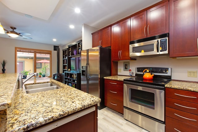 kitchen with sink, ceiling fan, appliances with stainless steel finishes, light stone counters, and light wood-type flooring