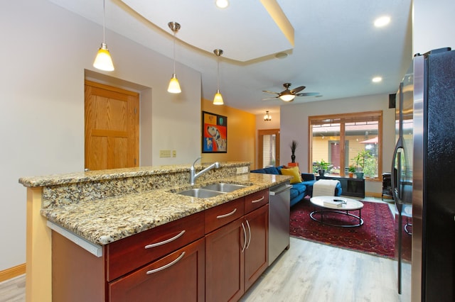 kitchen featuring appliances with stainless steel finishes, decorative light fixtures, sink, light stone countertops, and light wood-type flooring