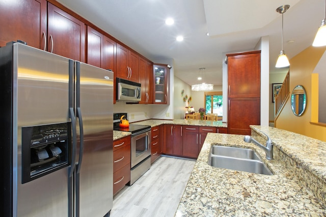 kitchen featuring pendant lighting, sink, stainless steel appliances, light stone countertops, and light wood-type flooring