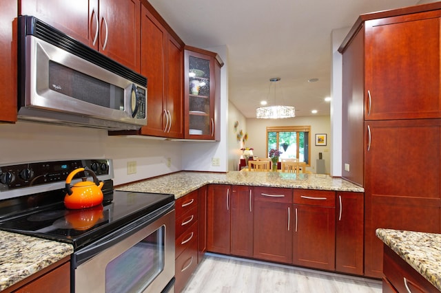 kitchen with light stone counters, hanging light fixtures, light wood-type flooring, kitchen peninsula, and stainless steel appliances