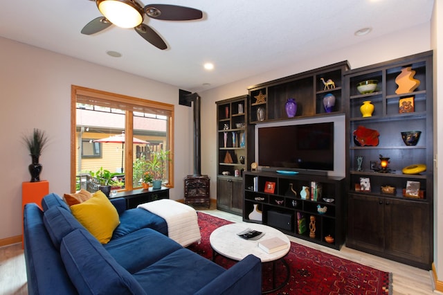 living room with ceiling fan, light hardwood / wood-style floors, and a wood stove