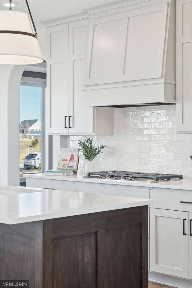 kitchen featuring stainless steel gas stovetop, white cabinetry, backsplash, and custom range hood