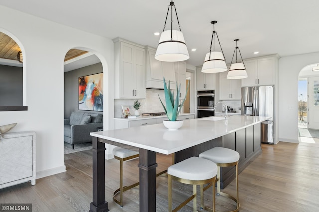 kitchen with a center island with sink, appliances with stainless steel finishes, decorative backsplash, decorative light fixtures, and white cabinets