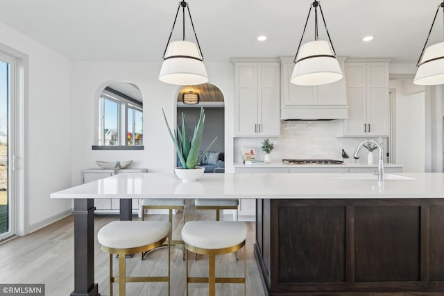 kitchen with white cabinetry, decorative backsplash, a spacious island, decorative light fixtures, and sink