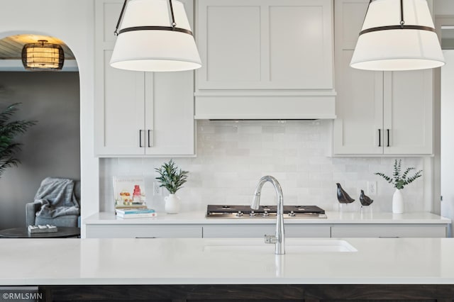 kitchen featuring custom exhaust hood, white cabinetry, decorative backsplash, and decorative light fixtures