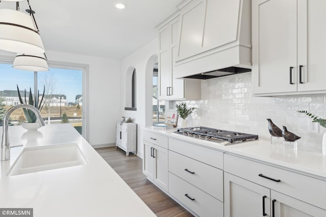 kitchen featuring sink, white cabinetry, hanging light fixtures, stainless steel gas cooktop, and custom range hood