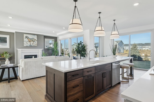 kitchen featuring a center island with sink, dishwasher, a high end fireplace, pendant lighting, and sink