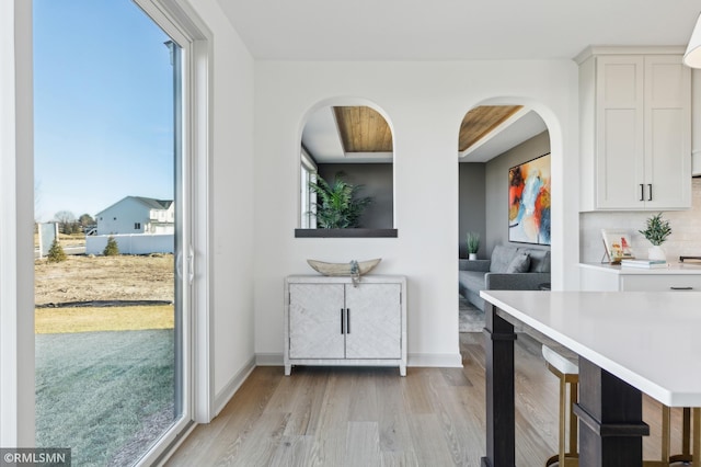 kitchen with light wood-type flooring, a breakfast bar area, white cabinetry, and backsplash