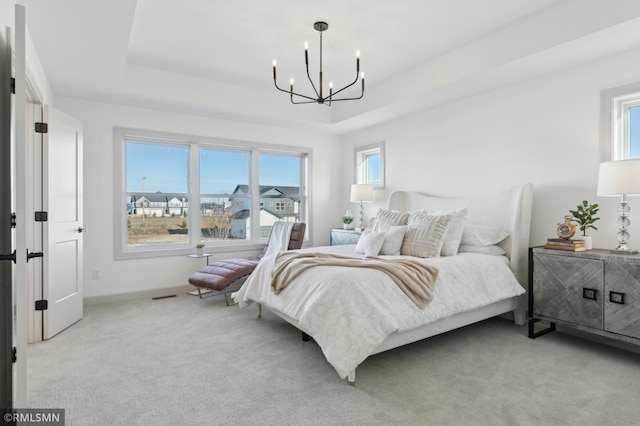 bedroom with light colored carpet, a tray ceiling, and a chandelier