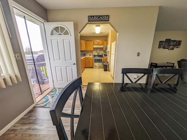 foyer with light wood-style floors, arched walkways, and baseboards