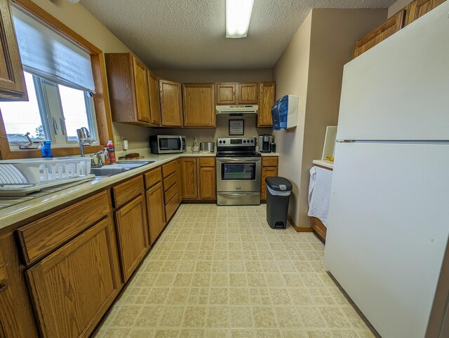 815 6th Ave NE, Perham, MN 56573 - kitchen featuring stainless steel appliances, under cabinet range hood, light countertops, brown cabinetry, and a textured ceiling