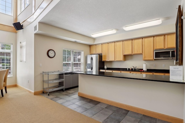 kitchen with a textured ceiling, light tile patterned flooring, stainless steel appliances, and a wealth of natural light