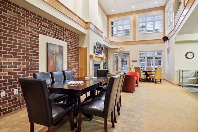 carpeted dining space with a high ceiling, brick wall, and a tiled fireplace