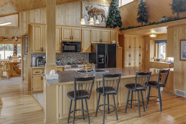 kitchen featuring wooden walls, black appliances, a kitchen island with sink, and sink