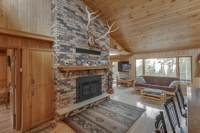 living room with wooden walls, light hardwood / wood-style flooring, a brick fireplace, and high vaulted ceiling