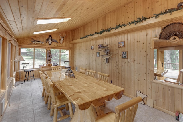 tiled dining space featuring lofted ceiling with skylight, wooden walls, and wood ceiling