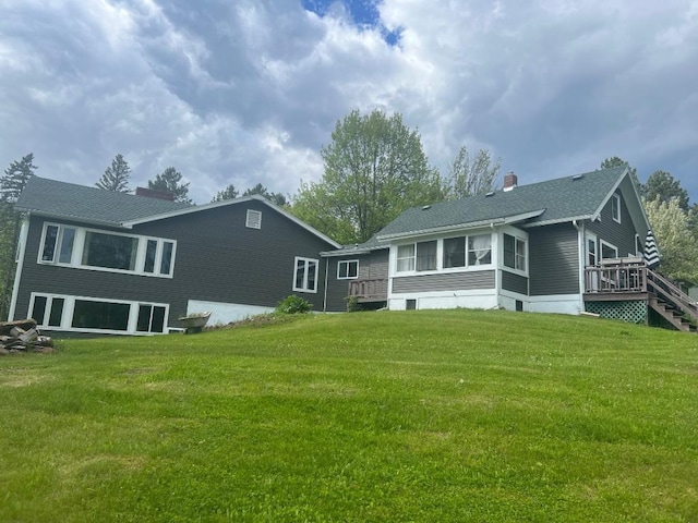 rear view of house featuring a lawn, a wooden deck, and a sunroom