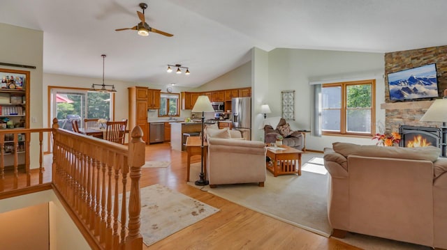 living room featuring a stone fireplace, light hardwood / wood-style flooring, sink, vaulted ceiling, and ceiling fan