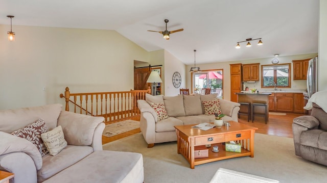 living room featuring light hardwood / wood-style flooring, a barn door, ceiling fan, and vaulted ceiling